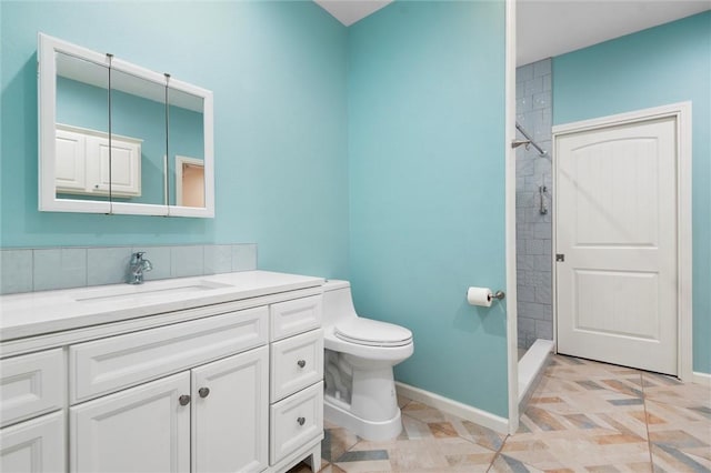 bathroom featuring toilet, vanity, baseboards, and a tile shower