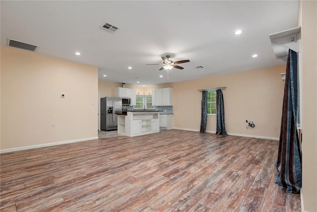 unfurnished living room featuring light wood finished floors, baseboards, visible vents, and a ceiling fan