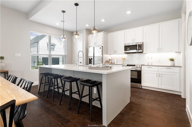 kitchen with a breakfast bar area, an island with sink, dark wood-style floors, backsplash, and stainless steel appliances