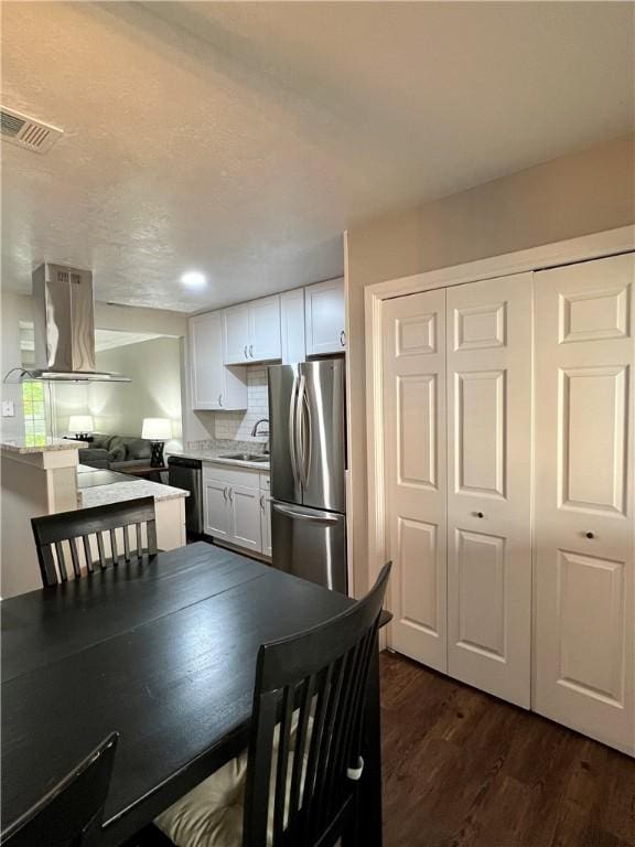 kitchen featuring sink, white cabinets, island exhaust hood, stainless steel refrigerator, and backsplash