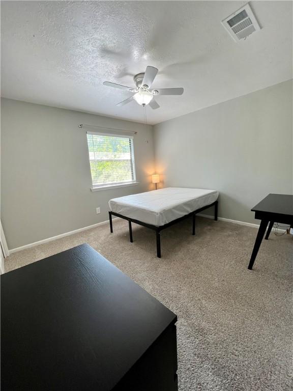 bedroom featuring ceiling fan, light colored carpet, and a textured ceiling