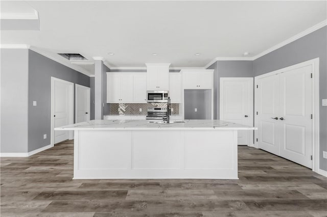 611 Levy St, Navasota, TX 77868 - kitchen with appliances with stainless steel finishes, white cabinets, an island with sink, baseboards, and ornamental molding