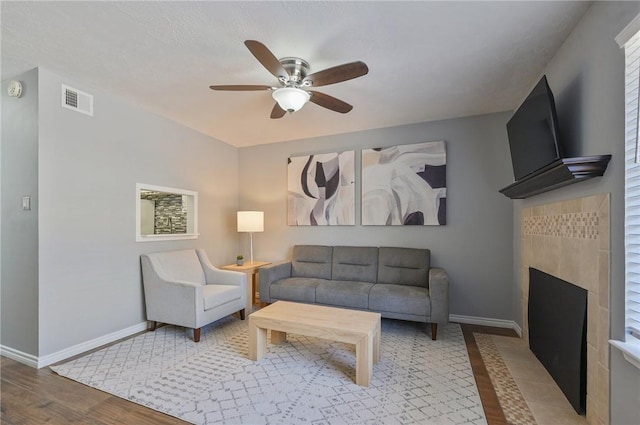 living room with ceiling fan, wood-type flooring, and a tile fireplace