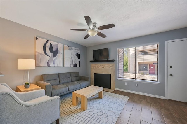 living room with hardwood / wood-style flooring, ceiling fan, a textured ceiling, and a tile fireplace