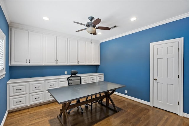 home office with crown molding, dark wood-type flooring, built in desk, and ceiling fan