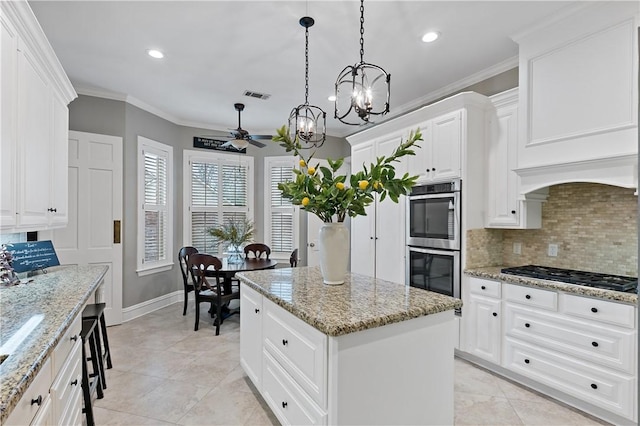 kitchen featuring appliances with stainless steel finishes, white cabinetry, hanging light fixtures, a center island, and light stone countertops