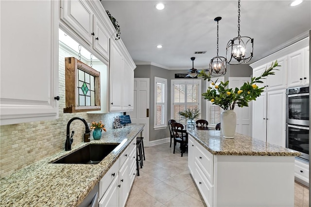 kitchen with sink, white cabinets, decorative backsplash, a center island, and light stone counters