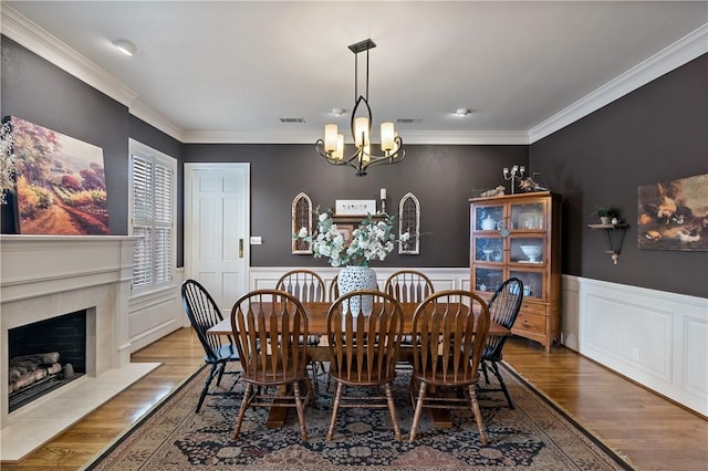 dining area featuring an inviting chandelier, hardwood / wood-style floors, crown molding, and a fireplace