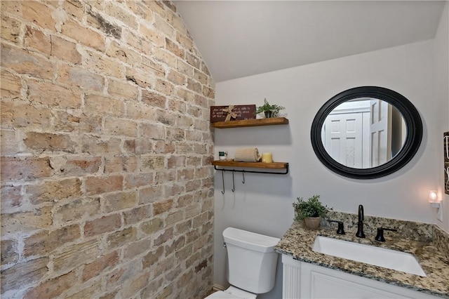 bathroom with lofted ceiling, vanity, toilet, and brick wall