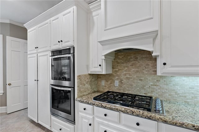 kitchen with appliances with stainless steel finishes, light stone counters, ornamental molding, white cabinets, and decorative backsplash