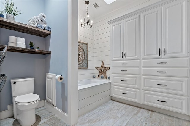 bathroom with hardwood / wood-style floors, a notable chandelier, a bathtub, and toilet