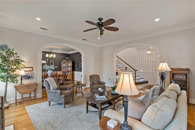 living room featuring ornamental molding, ceiling fan with notable chandelier, and light hardwood / wood-style flooring