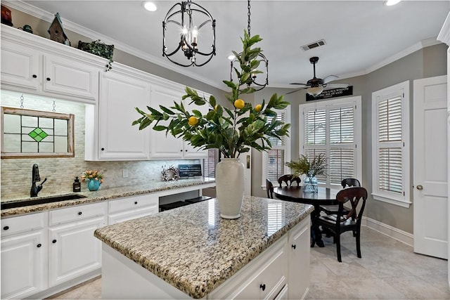 kitchen with white cabinetry, a kitchen island, sink, and pendant lighting