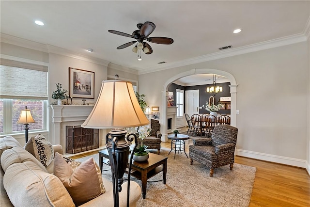 living room with crown molding, ceiling fan with notable chandelier, and light hardwood / wood-style floors