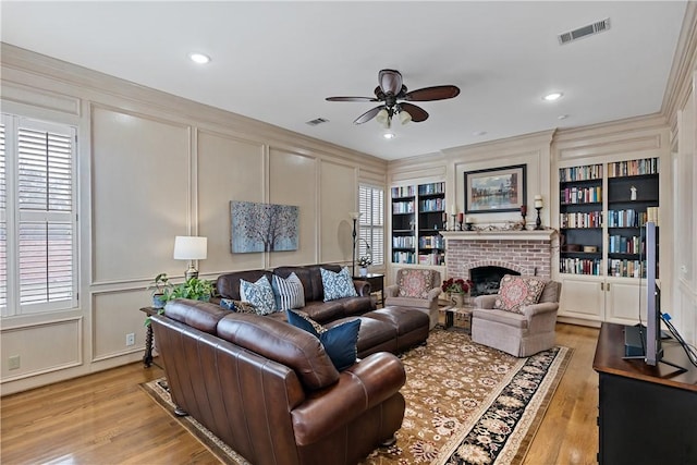 living room with a healthy amount of sunlight, ornamental molding, built in features, and light hardwood / wood-style flooring