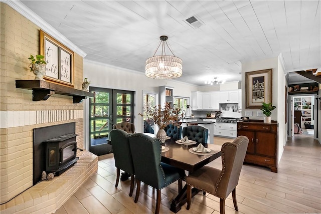 dining area with an inviting chandelier, ornamental molding, a wood stove, and light wood-type flooring