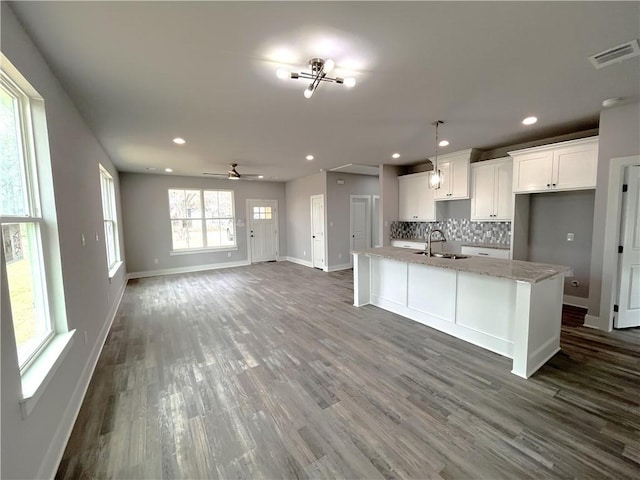 kitchen featuring visible vents, backsplash, a kitchen island with sink, a sink, and wood finished floors