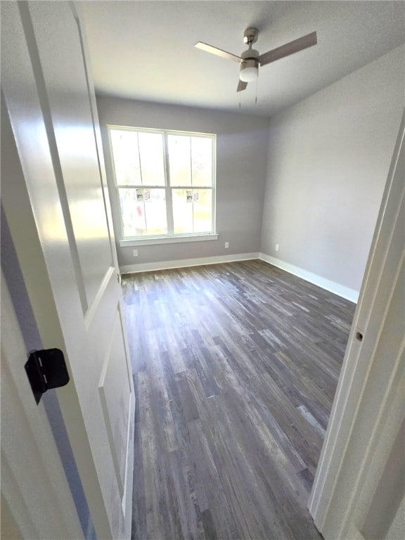 spare room with a ceiling fan, baseboards, and dark wood-style flooring