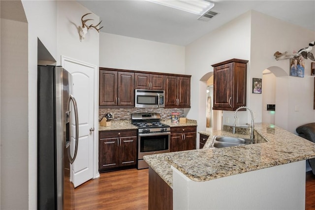 kitchen with visible vents, a peninsula, arched walkways, stainless steel appliances, and a sink