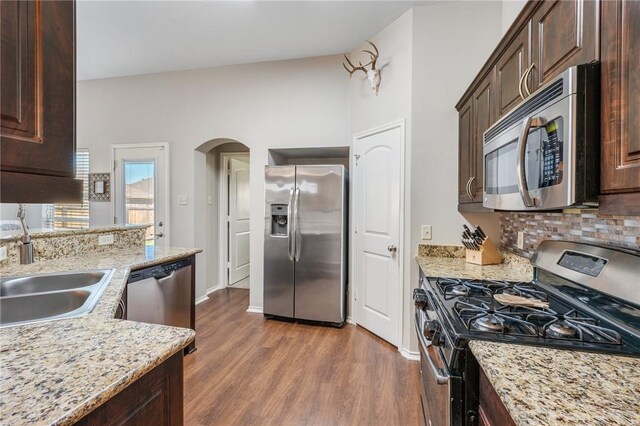 kitchen with dark brown cabinets, appliances with stainless steel finishes, arched walkways, dark wood-style floors, and a sink