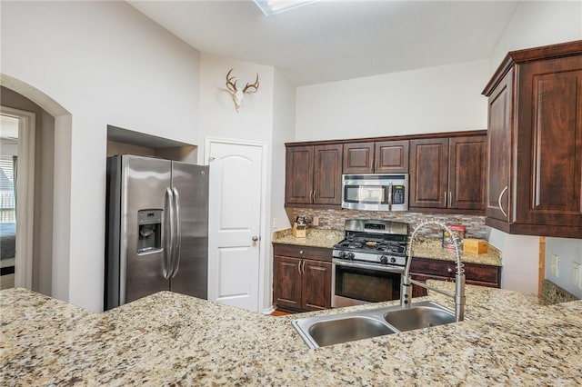 kitchen with decorative backsplash, appliances with stainless steel finishes, light stone countertops, and a sink