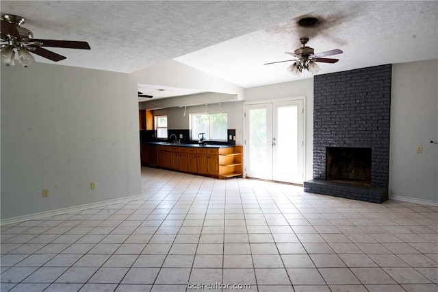 unfurnished living room with ceiling fan, french doors, a brick fireplace, a textured ceiling, and light tile patterned floors