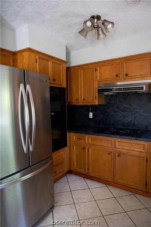 kitchen with light tile patterned floors, tasteful backsplash, stainless steel refrigerator, and dark stone countertops