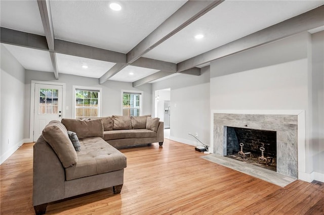 living room featuring beam ceiling, light wood-type flooring, and a tiled fireplace