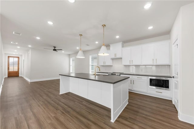 kitchen featuring built in microwave, sink, pendant lighting, a kitchen island with sink, and white cabinets