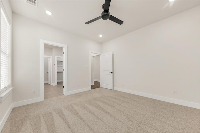 unfurnished bedroom featuring a spacious closet, light colored carpet, and ceiling fan