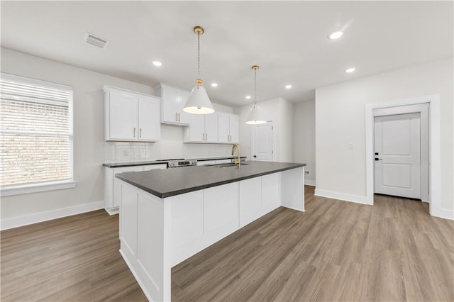 kitchen featuring white cabinetry, an island with sink, sink, hanging light fixtures, and light hardwood / wood-style floors