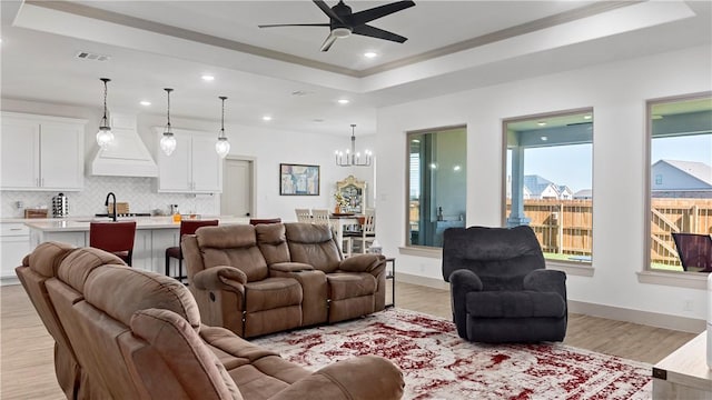 living room with ceiling fan with notable chandelier, light wood-type flooring, a tray ceiling, and ornamental molding