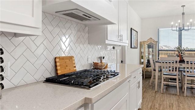 kitchen featuring pendant lighting, stainless steel gas stovetop, decorative backsplash, range hood, and white cabinetry