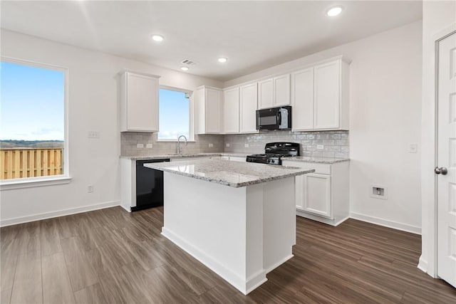 kitchen featuring black appliances, light stone counters, white cabinets, and a center island