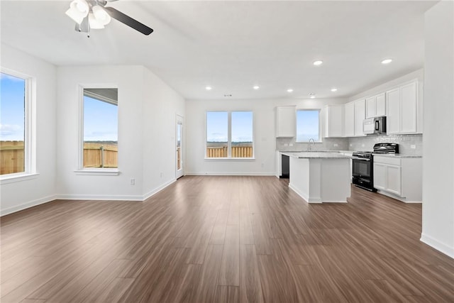 kitchen with white cabinetry, stainless steel microwave, open floor plan, and gas stove