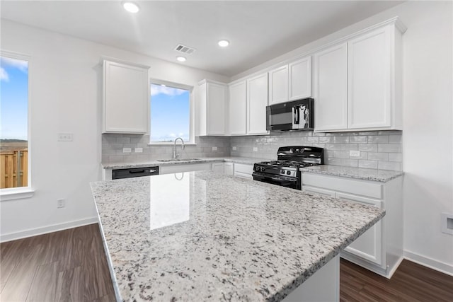 kitchen featuring light stone counters, white cabinetry, a sink, and black appliances