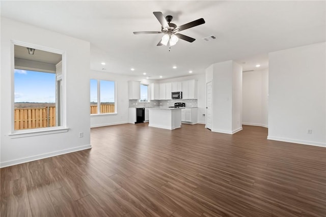 unfurnished living room with ceiling fan, dark wood-type flooring, visible vents, and baseboards