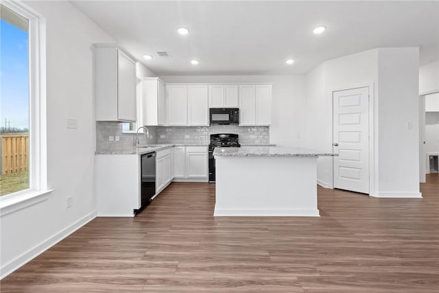 kitchen featuring black appliances, a kitchen island, white cabinetry, and light stone counters