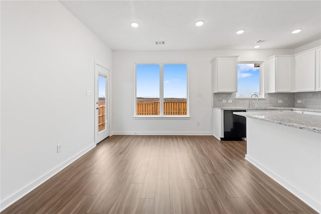 kitchen with dark wood-type flooring, white cabinets, backsplash, light stone countertops, and dishwasher