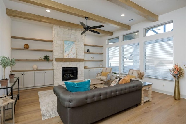 living room with beam ceiling, a stone fireplace, ceiling fan, and light wood-type flooring