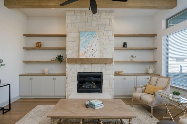 living room featuring ceiling fan, light wood-type flooring, a fireplace, and beam ceiling