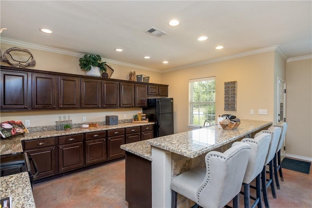 kitchen featuring dark brown cabinetry, light stone countertops, freestanding refrigerator, a peninsula, and a kitchen bar