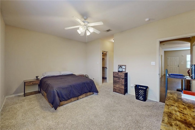 bedroom featuring a walk in closet, baseboards, carpet flooring, arched walkways, and a ceiling fan