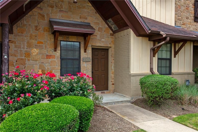 doorway to property featuring brick siding, stone siding, board and batten siding, and roof with shingles