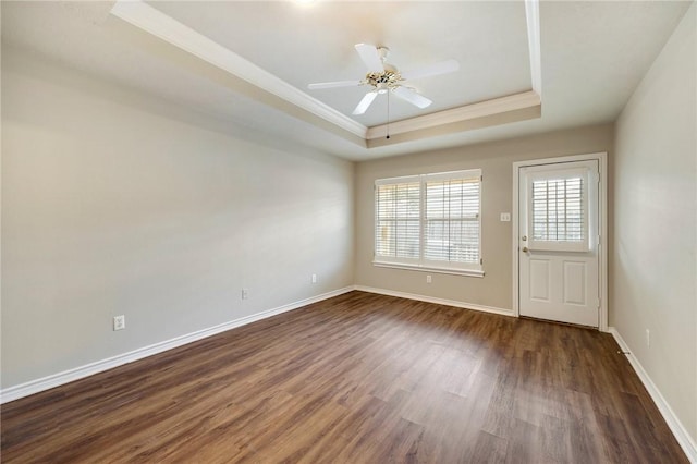 spare room with a tray ceiling, crown molding, dark wood-type flooring, a ceiling fan, and baseboards