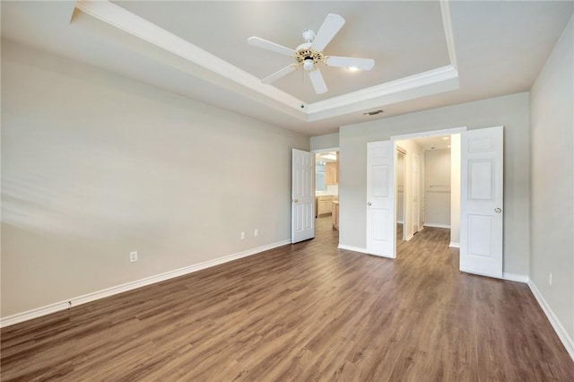 unfurnished bedroom with a raised ceiling, visible vents, a spacious closet, wood finished floors, and baseboards