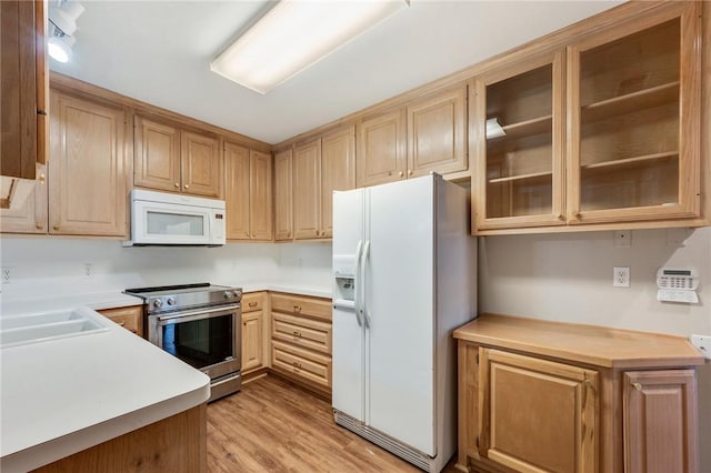 kitchen featuring light countertops, light wood-style floors, glass insert cabinets, a sink, and white appliances