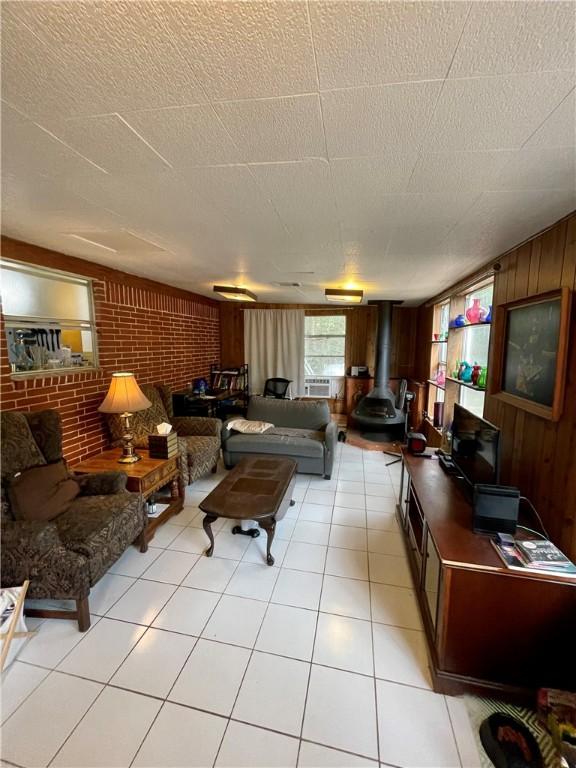 tiled living room with brick wall, wooden walls, a textured ceiling, and a wood stove