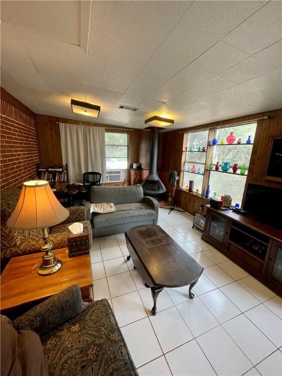 living room featuring wood walls, brick wall, light tile patterned floors, and a wood stove