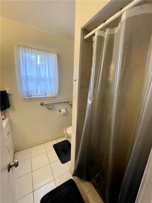 bathroom with toilet, curtained shower, and tile patterned flooring